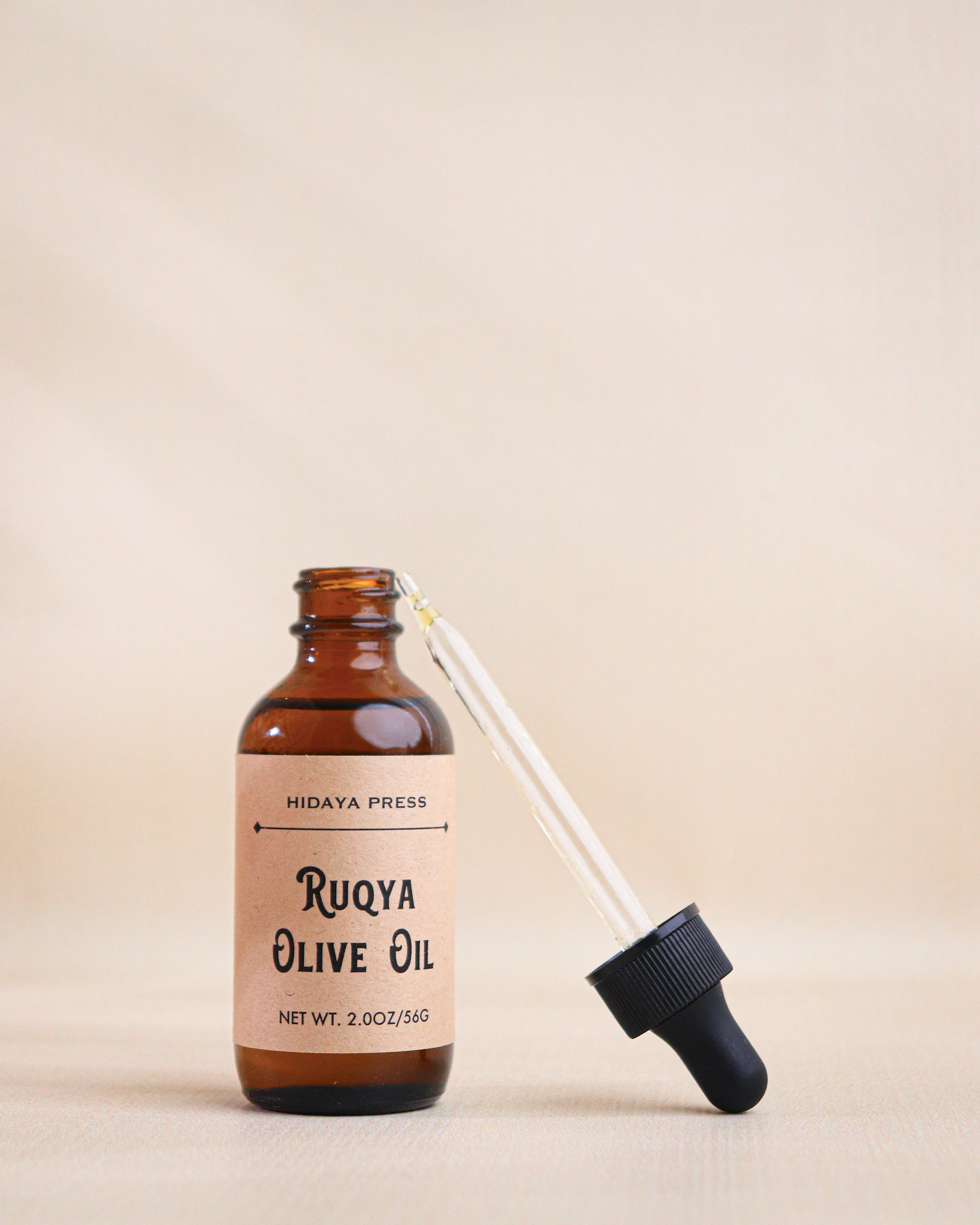 Brown glass bottle of Ruqya Olive Oil with a dropper on a beige background
