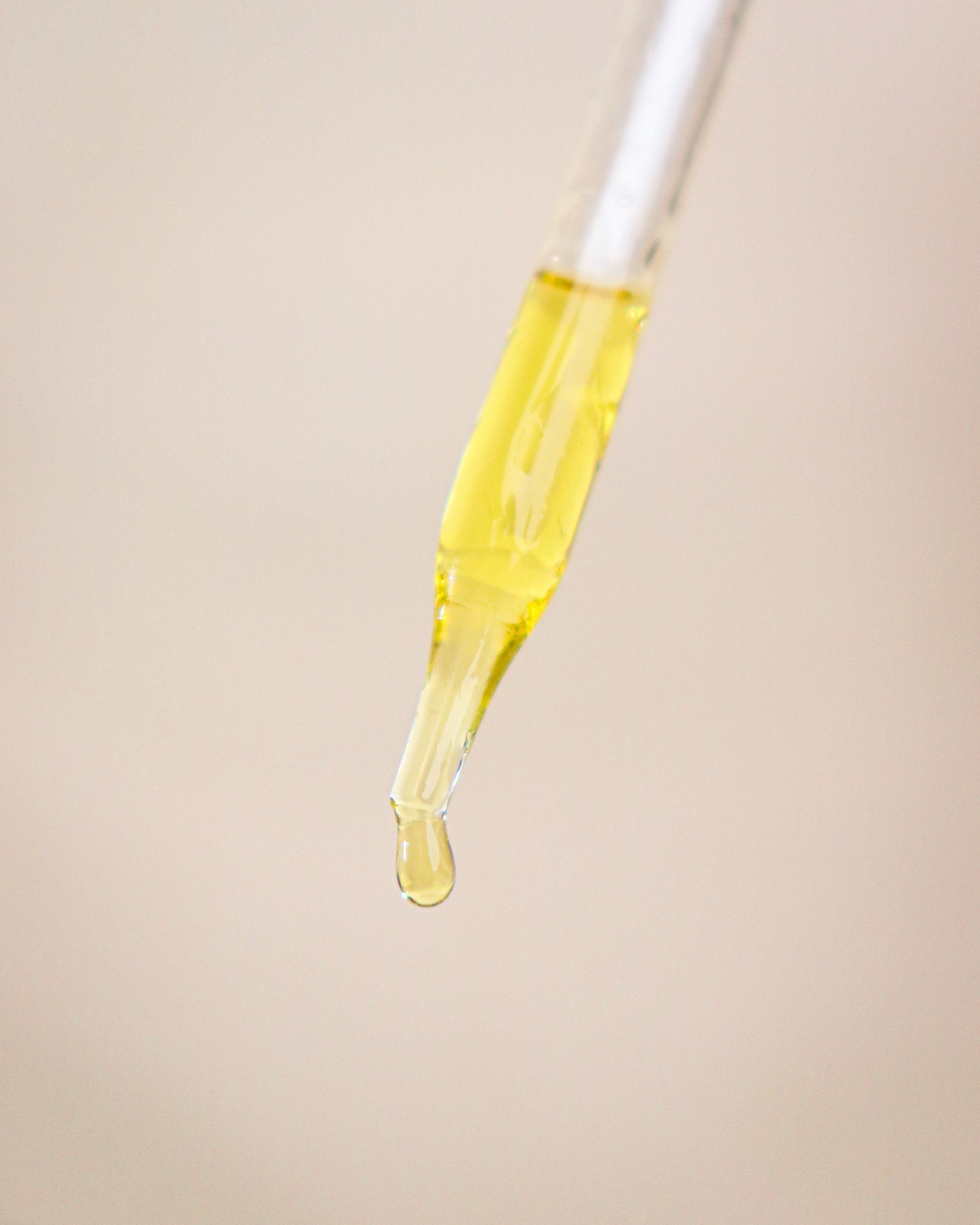Yellow oil being dripped from a glass dropper onto a beige background