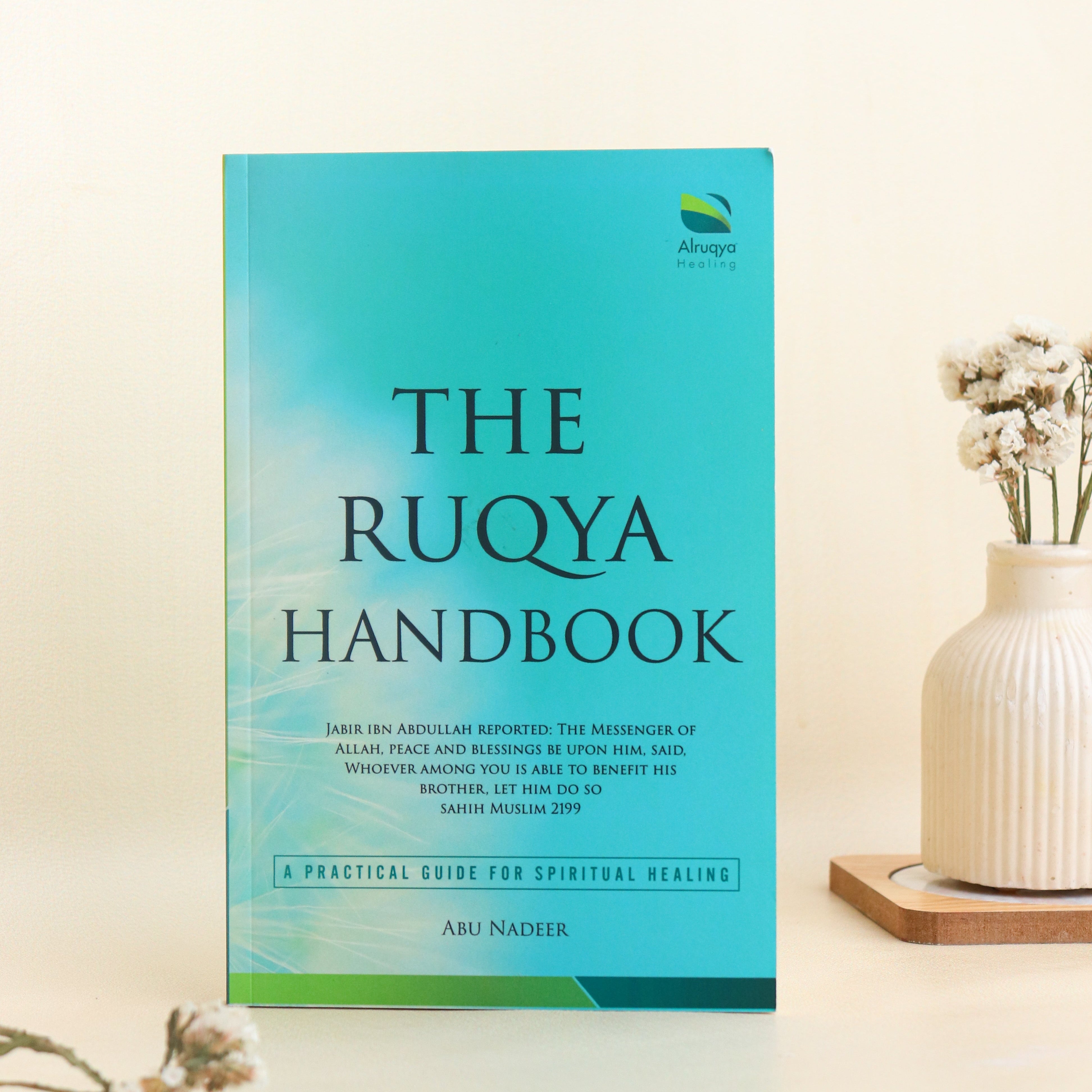 Book titled 'The Ruqya Handbook' on a light background with a vase and flowers.